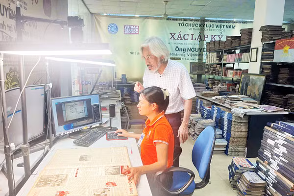 Nhà sưu tập Nguyễn Phi Dũng hướng dẫn chị Nguyễn Thị Hồng thực hiện việc chụp các trang Báo Nhân Dân. (Ảnh: MẠNH HÀO)