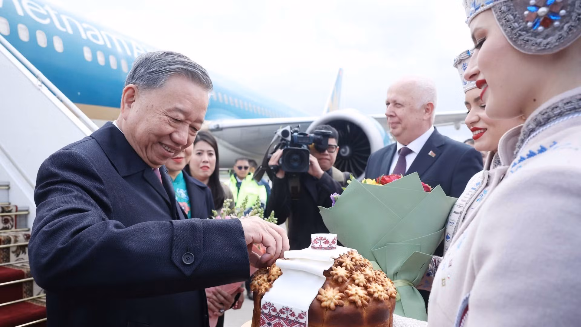 Thiếu nữ Belarus trong trang phục truyền thống trân trọng mời Tổng Bí thư Tô Lâm thưởng thức bánh mì và muối theo nghi thức đón khách quý của Belarus. (Ảnh: Thống Nhất/TTXVN)