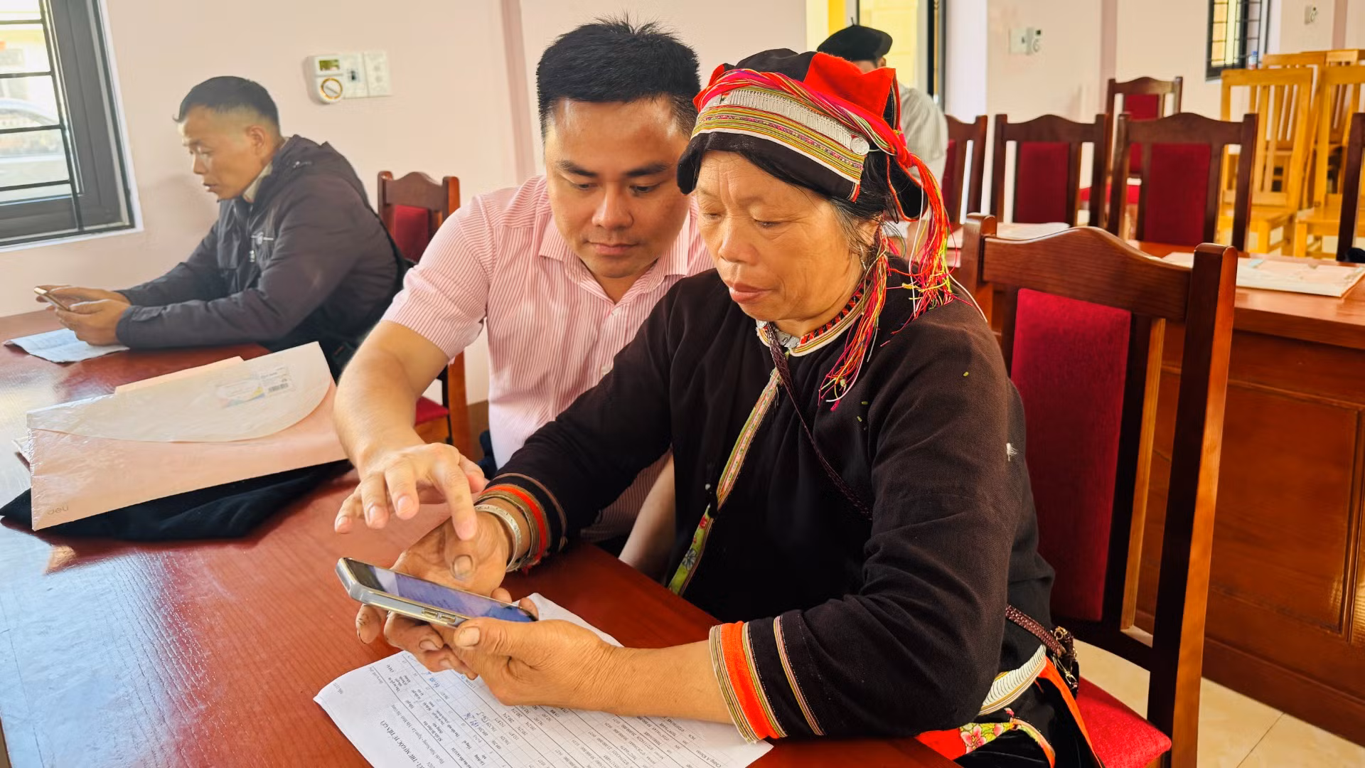 Cán bộ tín dụng hướng dẫn bà con cách truy cập ứng dụng của Ngân hàng Chính sách xã hội trên điện thoại để tra cứu các khoản vay.
