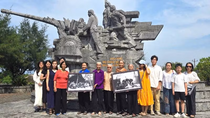 Gia đình nhà báo, liệt sĩ Lương Nghĩa Dũng chụp ảnh lưu niệm với các nữ pháo thủ bên tượng đài ghi dấu chiến công của Đại đội pháo binh Ngư Thủy.