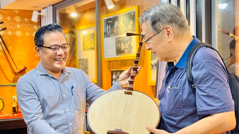 Nghệ sĩ Ưu tú Phan Quốc Kiệt (bìa trái), Giám đốc Nhà hát Cải lương Trần Hữu Trang tặng đoàn khách quốc tế cây đờn kìm. (Ảnh: Trung Sơn)