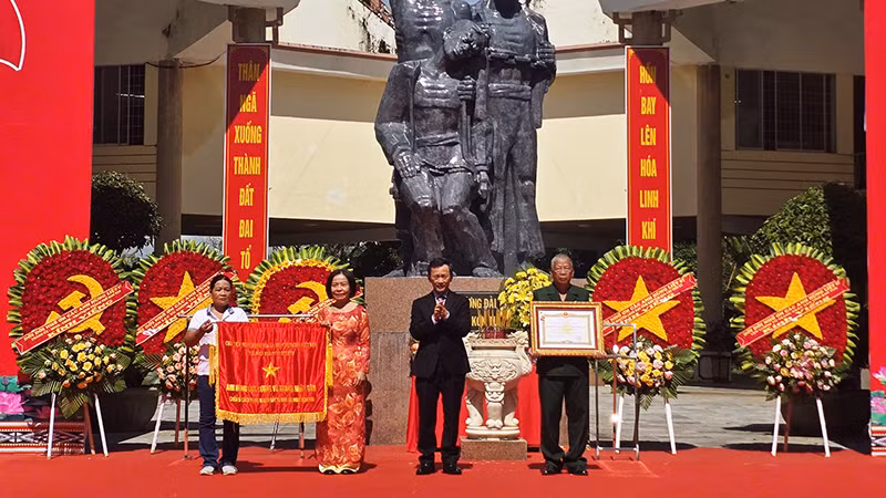 Đồng chí Dương Văn Trang trao tặng cờ và danh hiệu Anh hùng Lực lượng vũ trang nhân dân cho đại diện Tập thể chiến sĩ cách mạng bị địch bắt tù đày tại Ngục Kon Tum. 