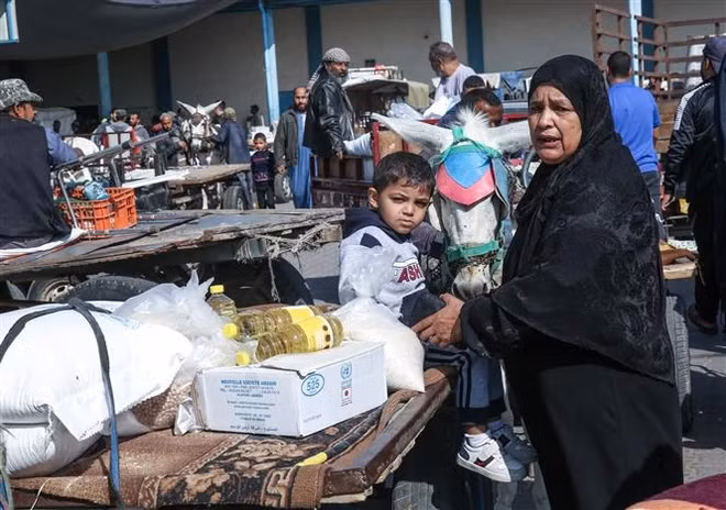 Người dân Palestine nhận lương thực cứu trợ tại một trung tâm phân phối của Cơ quan cứu trợ và hành động của Liên hợp quốc (UNRWA) tại trại tị nạn ở Rafah, Dải Gaza. (Ảnh: AFP/TTXVN)