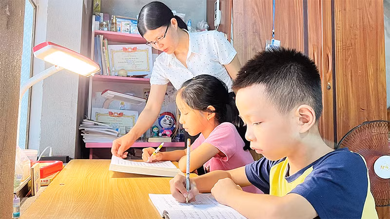 Mẹ đỡ đầu (Hội Phụ nữ phường An Phụ, thị xã Kinh Môn) hướng dẫn hai chị em Lương Thị Thanh Hiền và Lương Việt Hoàng làm bài tập. 