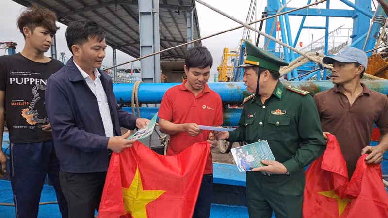 Đồng chí Nguyễn Bá Bình (thứ 2 từ trái qua phải), Phó Chính ủy Bộ đội Biên phòng tỉnh Bình Định trao cờ và tờ rơi tuyên truyền chống khai thác IUU cho ngư dân.