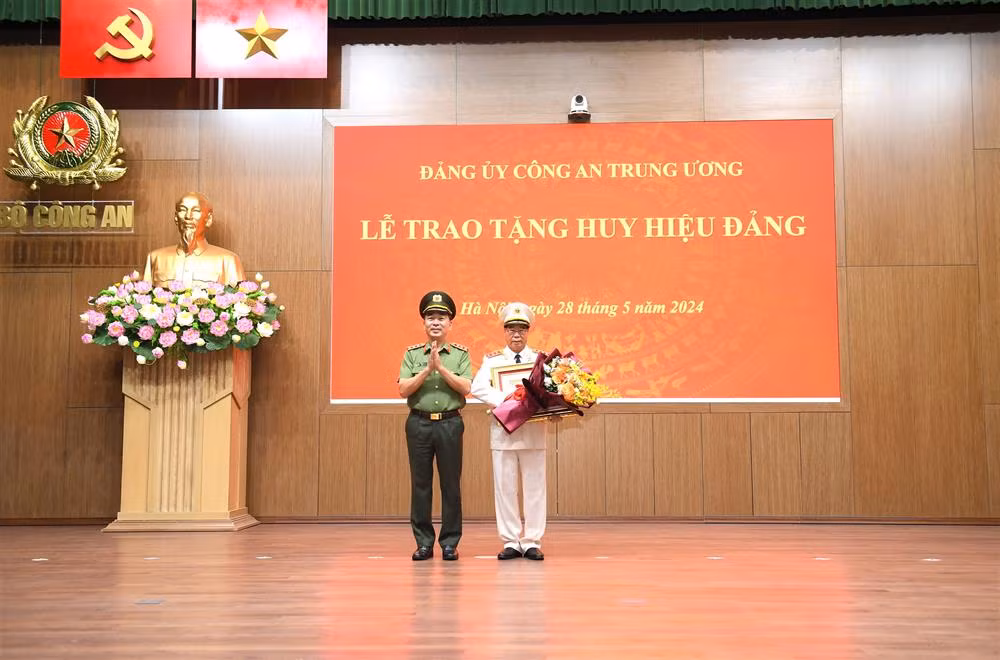Thứ trưởng Trần Quốc Tỏ trao Giấy chứng nhận, gắn Huy hiệu và tặng hoa chúc mừng Thượng tướng Bùi Văn Nam. (Ảnh: Bộ Công an)