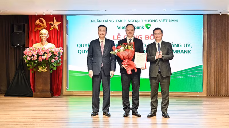 Đồng chí Phạm Quang Dũng, Ủy viên Ban Thường vụ Đảng ủy, Phó Thống đốc Ngân hàng Nhà nước (ngoài cùng bên trái) và đồng chí Nguyễn Thanh Tùng, Ủy viên Ban Chấp hành Đảng bộ Chính phủ, Bí thư Đảng ủy, Chủ tịch Hội đồng Quản trị Vietcombank (ngoài cùng bên phải) trao quyết định và tặng hoa chúc mừng đồng chí Lê Quang Vinh, tân Tổng Giám đốc Vietcombank.