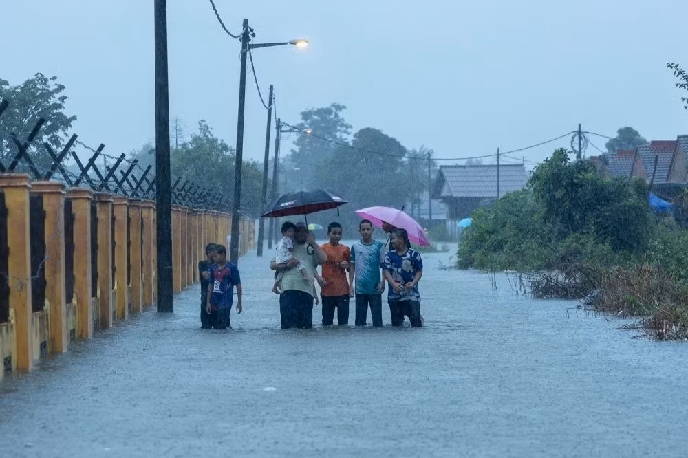 Người dân tại bang Kelantan đi bộ qua vùng lụt để tới Trung tâm cứu hộ. (Ảnh: Malaymail)