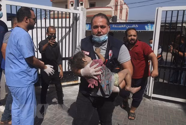 Người đàn ông ôm một em nhỏ bị thương sau cuộc không kích của Israel xuống Dải Gaza ngày 23/10/2023. (Ảnh: THX/TTXVN)