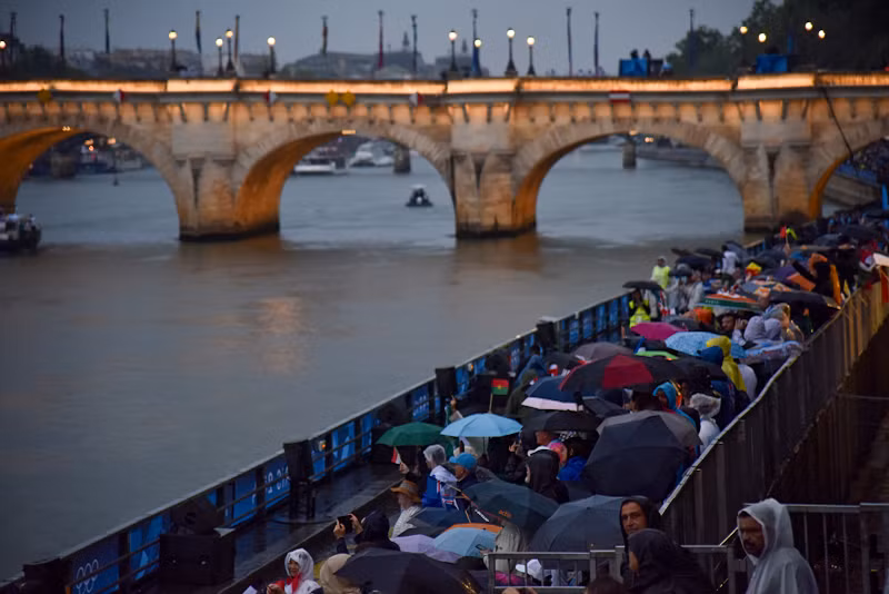Có rất nhiều thách thức cả về kỹ thuật và an ninh đối với nước chủ nhà khi tổ chức lễ khai mạc ngoài trời và trên sông. Chỉ những phút đầu tiên ngay khi bắt đầu lễ khai mạc, một cơn mưa ngoài ý muốn xuất hiện và có dấu hiệu nặng hạt dần, nhưng vẫn không xua tan đi được không khí náo nhiệt trên hàng ghế khán giả. (Ảnh: KHẢI HOÀN)