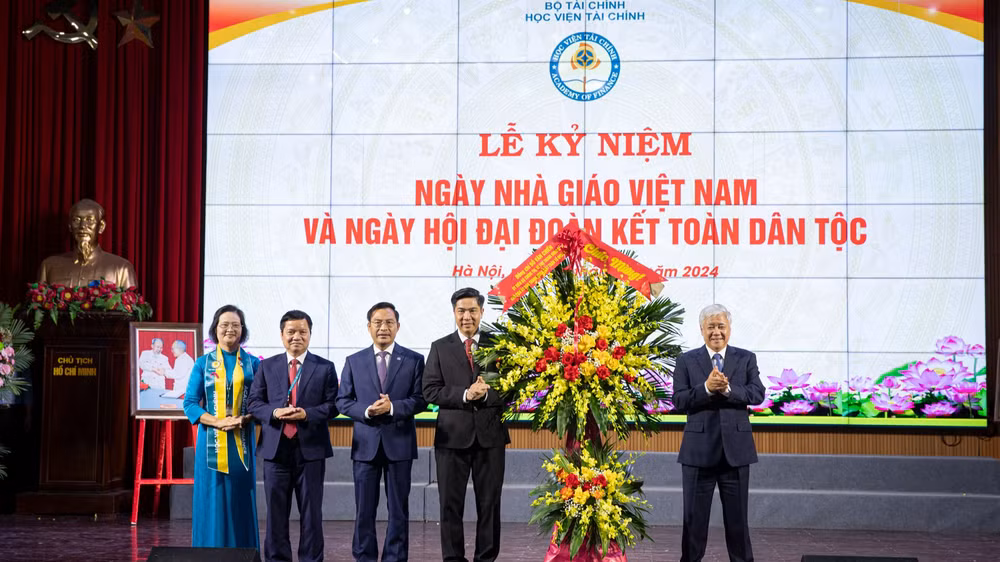 Đồng chí Đỗ Văn Chiến tặng hoa, chúc mừng các thầy giáo, cô giáo và toàn thể sinh viên Học viện Tài chính. (Ảnh: SƠN TÙNG)