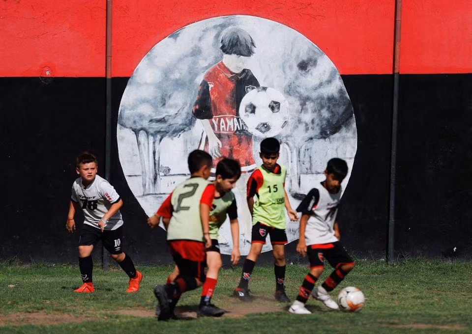 Các em nhỏ chơi bóng cạnh bức tranh tường về Messi trong trung tâm huấn luyện của câu lạc bộ Newell's Old Boys, đội bóng Messi đã từng chơi khi còn niên thiếu ở Rosario, Argentina. (Ảnh: Reuters)