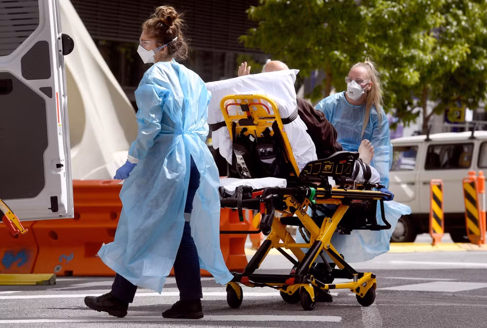 Nhân viên y tế chuyển bệnh nhân Covid-19 tới bệnh viện tại Melbourne, Australia. (Ảnh: AFP/TTXVN)