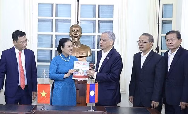 Bà Nguyễn Phương Nga tặng Chủ tịch Ủy ban Hòa bình và Đoàn kết Lào Sommad Pholsena cuốn đặc san "60 năm hữu nghị Việt Nam-Lào: Chung dãy Trường Sơn" của Tạp chí Thời Đại. (Nguồn: Báo Hà Nội mới)