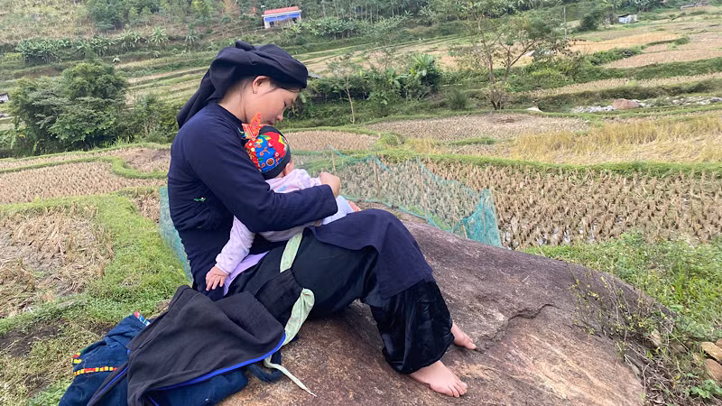 Những đứa trẻ được nghe mẹ hát ru khi theo mẹ đi làm. (Trong ảnh: Một phụ nữ ở xã Giáo Hiệu hát ru trẻ khi đi làm đồng). (Ảnh: THU TRANG)