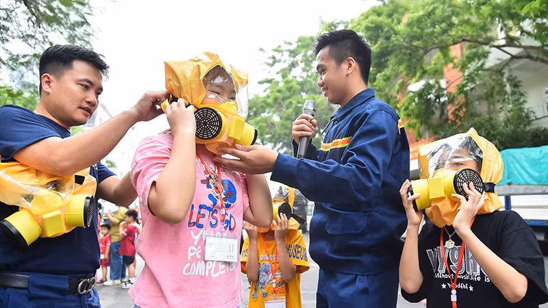 Cán bộ, chiến sĩ Trường đại học Phòng cháy chữa cháy hướng dẫn các gia đình sử dụng mặt nạ cứu hỏa đa năng Chance E và trải nghiệm mô hình thoát hiểm nhà khói. (Ảnh MỸ HÀ)