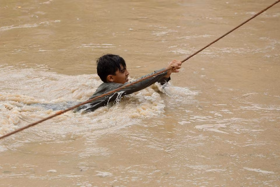 Cậu bé vượt qua con đường bị ngập nhờ sự giúp đỡ của sợi dây thừng. (Ảnh: Reuters)
