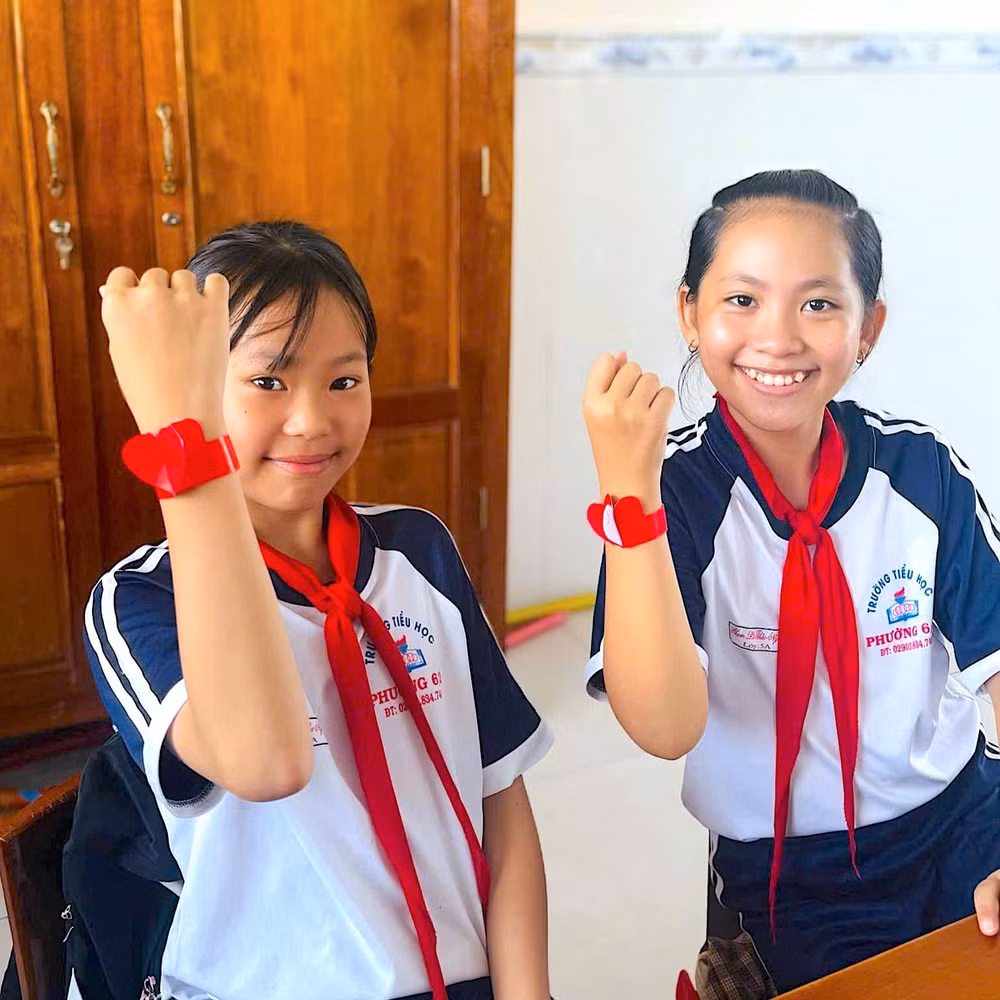 Hai bạn nhỏ Cà Mau trong đồng phục học sinh với điểm nhấn đồng hồ thể hiện tình yêu quê hương, đất nước.