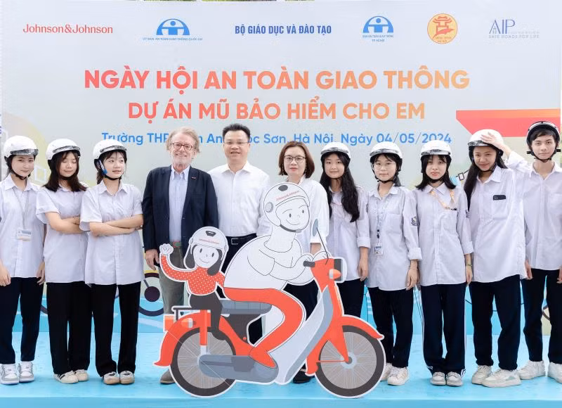 Ông Greig Craft, Chủ tịch Quỹ AIP, ông Lê Kim Thành, Phó Chủ tịch chuyên trách Ủy ban An toàn giao thông Quốc gia và đại diện Johnson&amp;Johnson Việt Nam tặng mũ bảo hiểm cho các em học sinh.