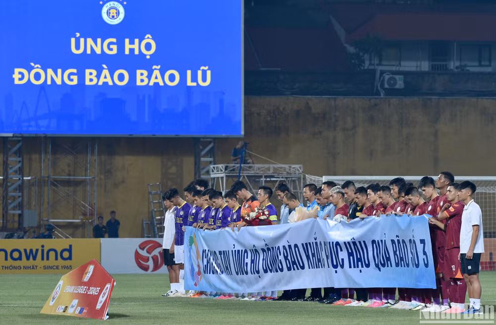 Các cầu thủ và khán giả tại sân Hàng Đẫy dành phút mặc niệm tới những người đã mất do ảnh hưởng của bão số 3 vừa qua. (Ảnh: TRẦN HẢI)