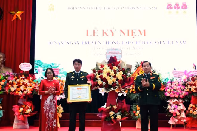 Trung tướng Nguyễn Hữu Chính tặng hoa chúc mừng và trao Bằng khen của Trung ương Hội Nạn nhân chất độc da cam/dioxin Việt Nam cho Tạp chí Da cam Việt Nam. 