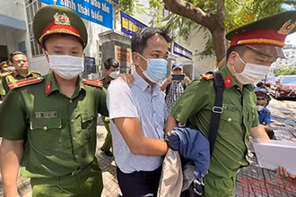 Cảnh sát áp giải ông Trần Quốc Huy, Trưởng Phòng Tổ chức-Hành chính CDC Khánh Hòa rời khỏi trụ sở làm việc. (Ảnh: THÀNH LONG)