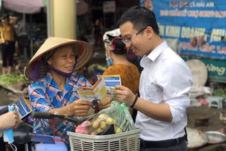 Người dân được phát tờ rơi và tư vấn về chính sách BHXH, BHYT. Ảnh: TÂM TRUNG.