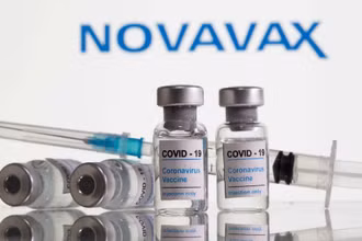 Các lọ dán nhãn vaccine ngừa Covid-19 và ống tiêm được nhìn thấy phía trước logo Novavax. (Ảnh: Reuters).