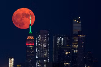 Trăng tròn màu cam đỏ mọc sau Tòa nhà Empire State ở thành phố New York, Mỹ tối 23/7. Ảnh: Reuters.