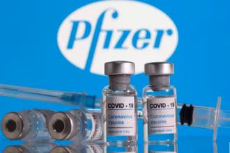 Lọ vaccine ngừa Covid-19 đặt trước logo Pfizer được chụp vào ngày 9-2. Ảnh: Reuters.
