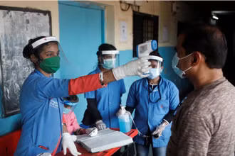 Nhân viên y tế đo thân nhiệt cho người dân tại một trường học ở Mumbai, Ấn Độ, ngày 10-8. (Ảnh: Reuters)