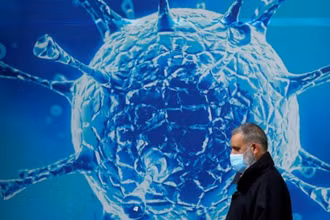 Người dân đeo khẩu trang đi ngang qua hình ảnh minh họa cho virus SARS-CoV-2. (Ảnh: Reuters)