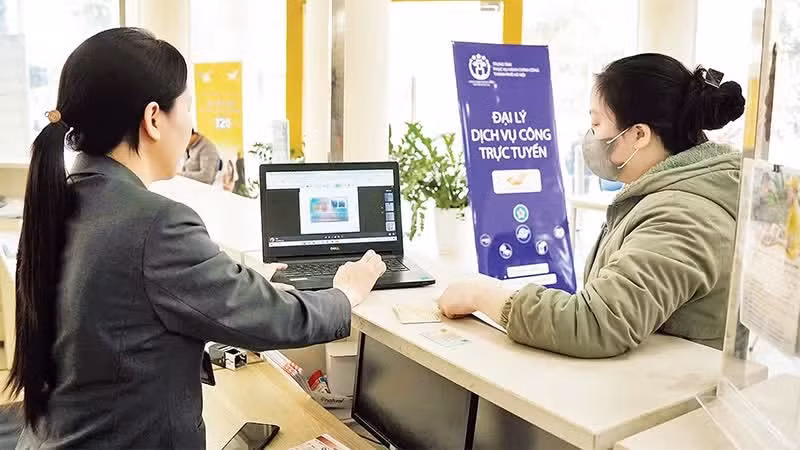 Người dân được nhân viên hướng dẫn làm thủ tục hành chính tại các đại lý dịch vụ công trực tuyến của thành phố Hà Nội. (Ảnh: NGUYÊN TRANG)