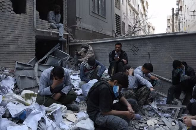 Người dân Iran bên những toà nhà đổ nát sau các cuộc không kích của Mỹ và Israel xuống thủ đô Tehran ngày 15/3/2026. (Ảnh: THX/TTXVN)