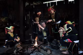 Bà Bàn Minh Toan cùng các phụ nữ Dao Lù Gang quây quần bên bếp lửa thực hiện công đoạn sơn đầu, trong không gian sinh hoạt đậm chất cộng đồng.