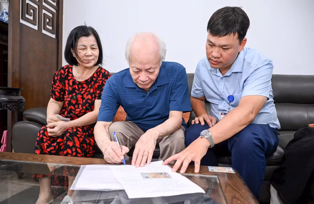Anh Lê Minh Thiện (phải) hỗ trợ ông Nguyễn Xuân Bình làm thủ tục ủy quyền lương hưu. Ảnh: Thành Đạt 