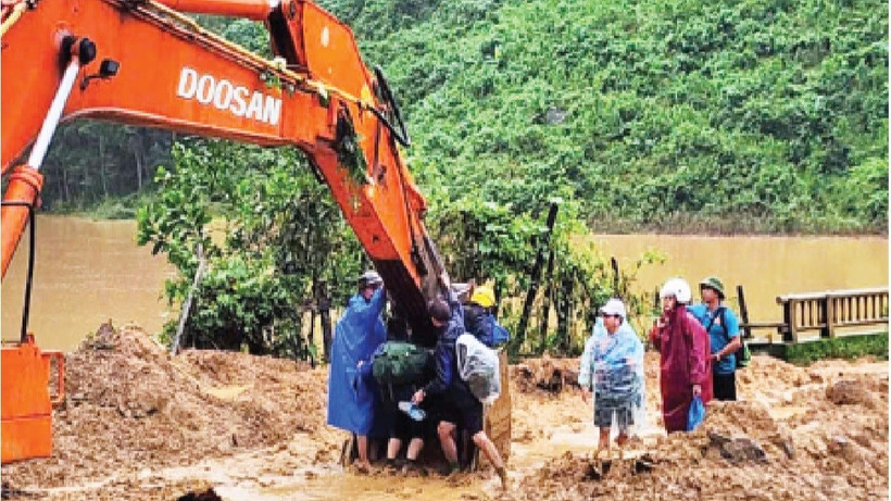 Các thầy, cô giáo ở xã Phước Chánh phải ngồi trên gàu của xe múc để vượt qua chỗ sạt lở vào trường học. (Ảnh: ANH QUÂN)