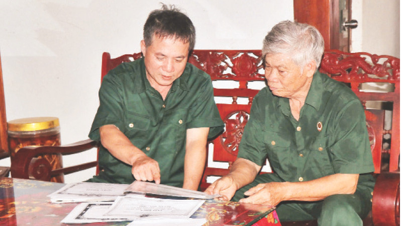 Ông Nguyễn Xuân Tạc (bên phải) giới thiệu về “tài sản” của mình là những giấy khen các em học sinh trong ấp cung cấp để nhận thưởng. 