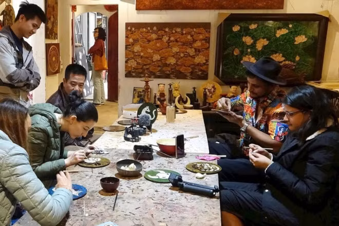 Du khách nước ngoài trải nghiệm làm sơn mài ở làng Hạ Thái. (Ảnh: LÊ BÍCH)