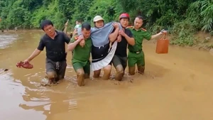 Công an xã Hữu Kiệm dìu sản phụ Kha Thị May vượt bùn lũ đến trạm y tế. (Ảnh: NGÔ HÙNG)
