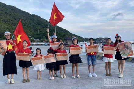 Du khách tham quan đảo Cù Lao Chàm, thành phố Đà Nẵng và ghi lại hình ảnh đáng nhớ với ấn phẩm phụ san đặc biệt kỷ niệm 80 năm Quốc khánh của Báo Nhân Dân trao tặng. (Ảnh: TÙNG LÂM)
