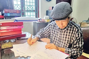 Nhà văn Minh Chuyên miệt mài bên trang bản thảo. (Ảnh: HẢI NAM)