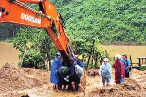 Các thầy, cô giáo ở xã Phước Chánh phải ngồi trên gàu của xe múc để vượt qua chỗ sạt lở vào trường học. (Ảnh: ANH QUÂN)