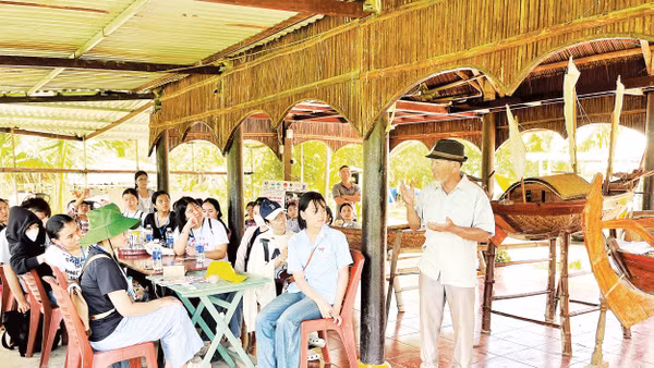 Du khách lắng nghe kể chuyện giữ gìn nghề đóng ghe bầu tại Làng mộc Kim Bồng.