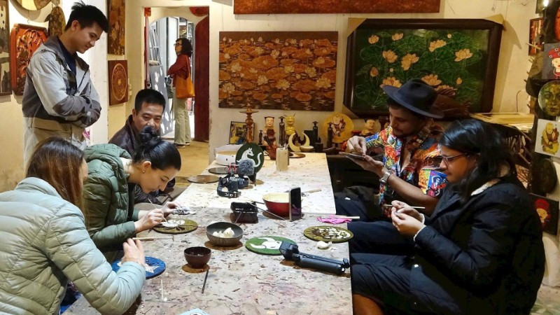 Du khách nước ngoài trải nghiệm làm sơn mài ở làng Hạ Thái. (Ảnh: LÊ BÍCH)
