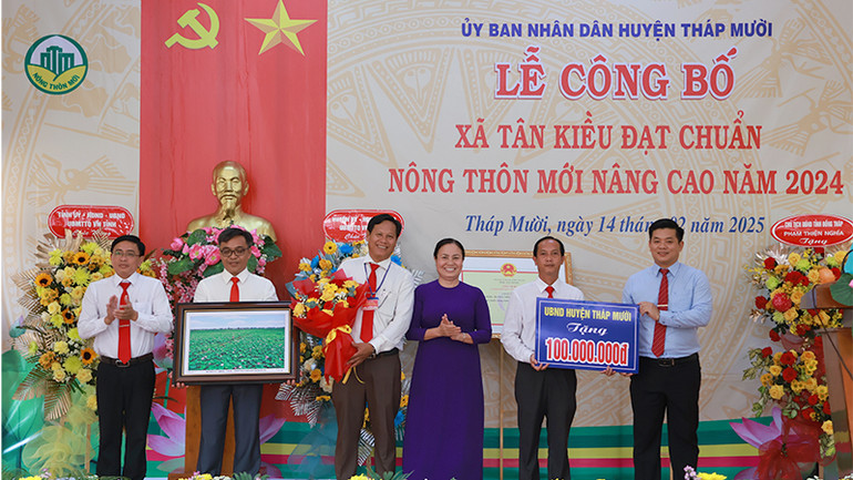 Lãnh đạo Huyện ủy, Ủy ban nhân dân huyện Tháp Mười trao bảng tượng trưng công trình phúc lợi trị giá 100 triệu đồng và tặng hoa chúc mừng. (Ảnh: HOÀNG KHA)