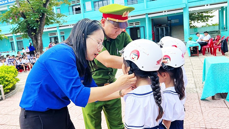 Giáo viên và cán bộ Công an hướng dẫn học sinh đội mũ bảo hiểm đúng cách.