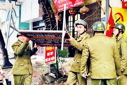 Lực lượng chức năng xã Nam Phù xử lý các biển hiệu quảng cáo lấn chiếm vỉa hè. (Ảnh NGHIÊM XUYÊN)