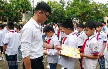 Cán bộ bảo hiểm phát tờ rơi tuyên truyền về bảo hiểm y tế học sinh. (Ảnh: TTXVN)