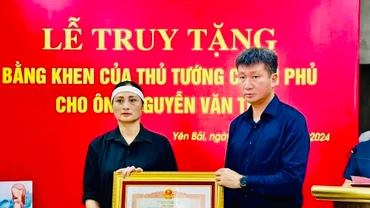 Chủ tịch Ủy ban nhân dân tỉnh Yên Bái Trần Huy Tuấn trao Bằng khen của Thủ tướng Chính phủ cho gia đình anh Nguyễn Văn Thi. (Ảnh: THANH SƠN)
